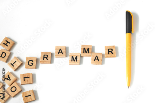 Top view of pen and words learn grammar made of square wooden tiles with the English alphabet scattered on a white background with space for text. The concept of thinking development, grammar.