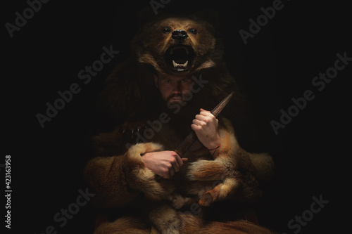Foto A male shaman werewolf in the skin of a bear sits in a dark room and reflects