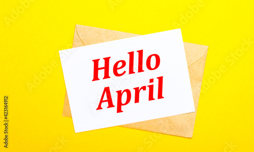 On a yellow background, an envelope and a card with the text HELLO APRIL. View from above