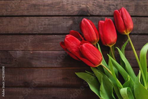 bouquet of red tulips lying on brown plank background
