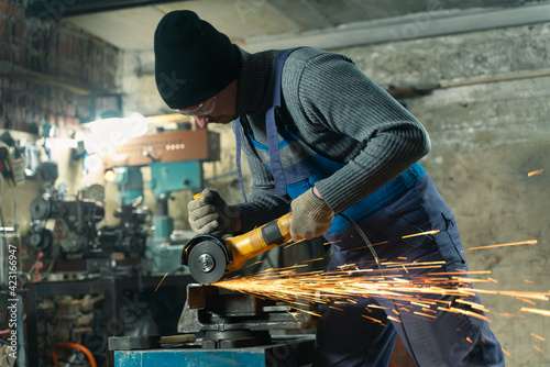 Locksmith in special clothes and goggles works in production. Metal processing with angle grinder. Sparks in metalworking