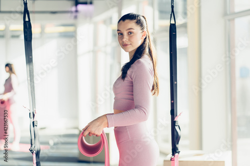 Healthy attractive young causian woman looking at camera, rolling up yoga mat after exercising and doing meditation at fitness gym studio. Sportive people unrolling mat preparing for fitness workout. photo