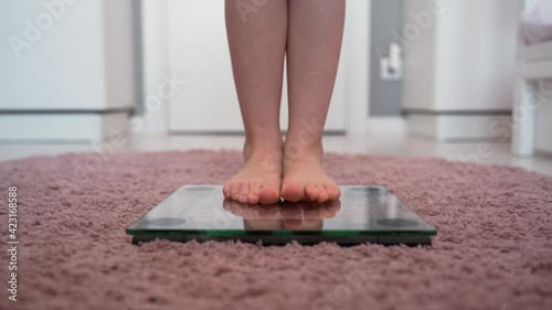The legs of the child on the scales. A little girl gets bare feet on the scales. Scales on pink carpet. The concept of weight loss and excess weight in children. Good and correct weight for the child