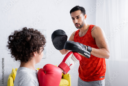 Arabian man in punch mitts training with son in boxing gloves on blurred foreground © LIGHTFIELD STUDIOS
