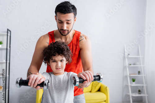 Concentrated arabian boy training with dumbbells near father at home