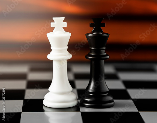 White and black chess pieces of kings and queens stand on a battle chessboard on a red wooden background