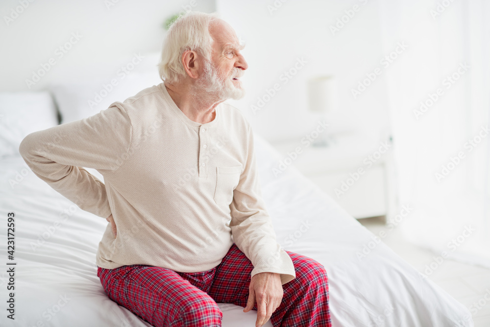 Photo of unhappy upset mature man nightwear sitting bed felling pain back indoors inside room home Photo of unhappy upset mature man nightwear sitting bed felling pain back indoors inside room home