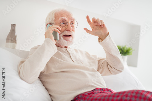 Photo of elderly man pensioner call talk cellphone mobile conversation listen speak talk sit bed wear pajamas indoors