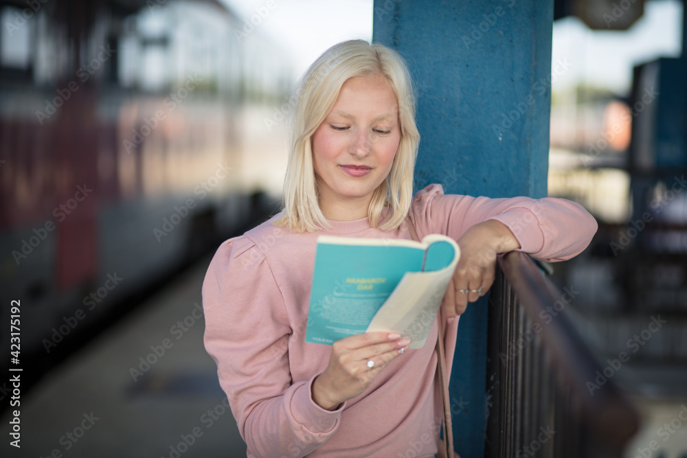Young lady reading book, waiting for a train.