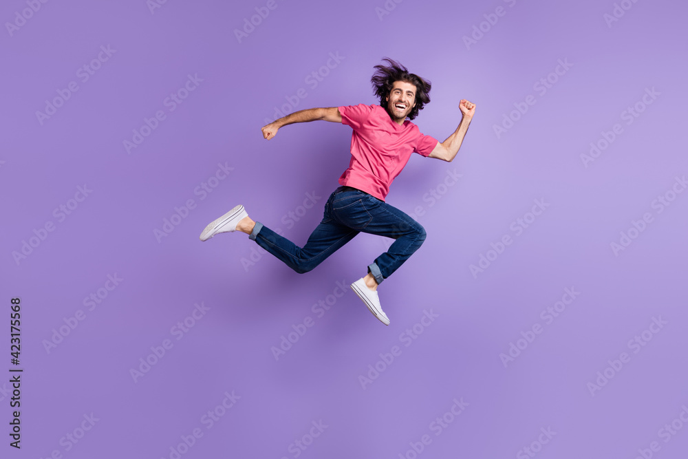 Full size profile photo of optimistic nice brunet guy jump wear pink t-shirt jeans isolated on violet background