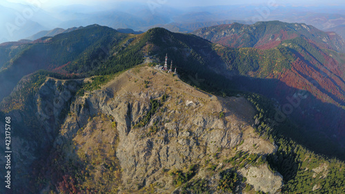 A GSM tower placed on top of a craggy mountain peak, near a steep abyss. Beyond the cliffs of Cozia mountains, lays Olt valley and the neighboring Capatanii Massif. Carpathia, Romania.