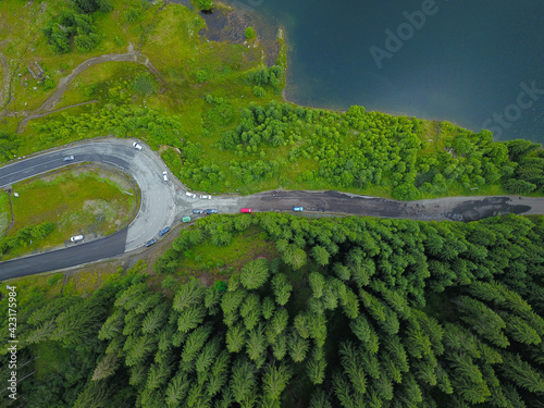 Aerial drone view of a crossroad near a lake. The road is located in a mountainous area, and crosses dense spruce forests. Rainy summer day. Carpathia, Romania