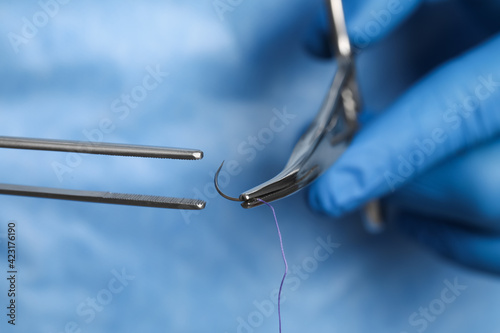 Professional surgeon holding forceps with suture thread, closeup. Medical equipment