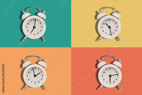 Four alarm clocks on a colored background. The hands of the clock show different times. Flat lay