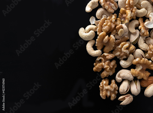 mixture of nuts (peanuts, pistachios, almonds, walnuts, hazelnut, cashew) from top view with black background with copy space