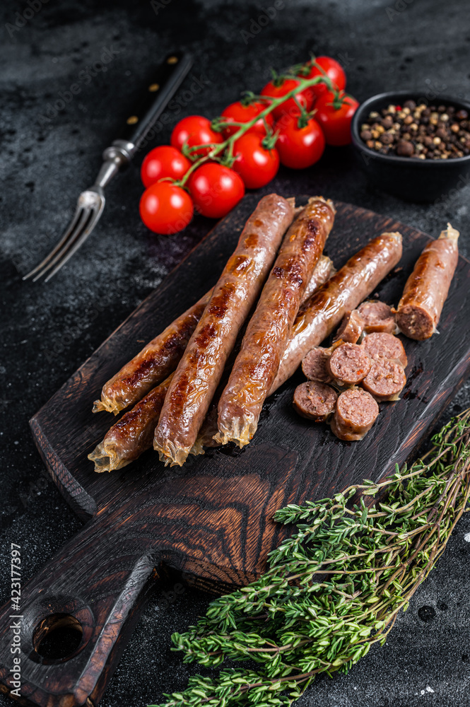 Roasted meat sausage on a wooden board with herbs and tomato. Black background. Top view