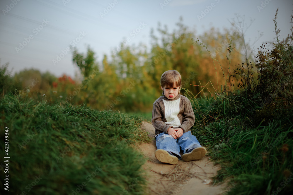 Sad boy child sits on a path in the park in the forest, a lonely child. Concept Children's emotions and psychology Sad boy child sits on a path in the park in the forest, a lonely child. Concept Children's emotions and psychology