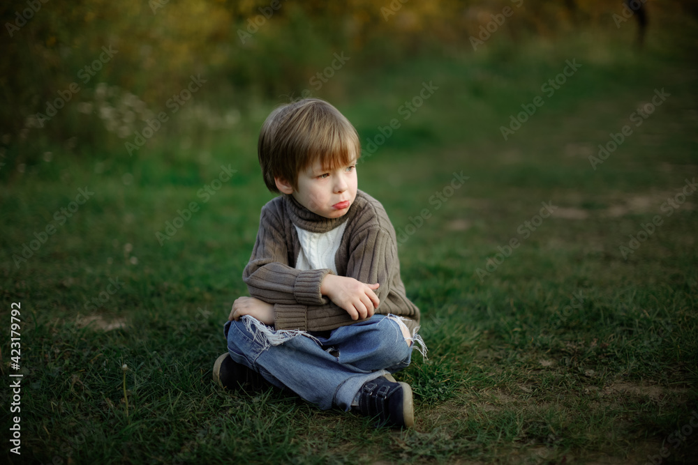 Sad boy child sits on a path in the park in the forest, a lonely child. Concept Children's emotions and psychology Sad boy child sits on a path in the park in the forest, a lonely child. Concept Children's emotions and psychology