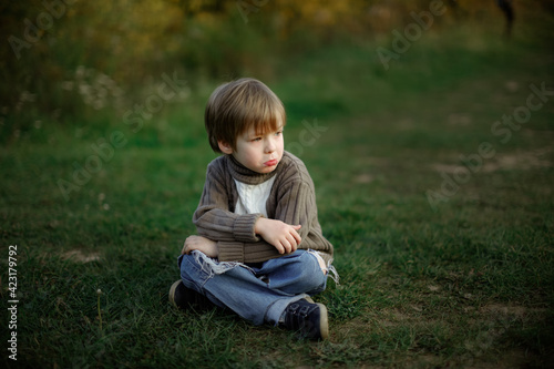 Sad boy child sits on a path in the park in the forest, a lonely child. Concept Children's emotions and psychology