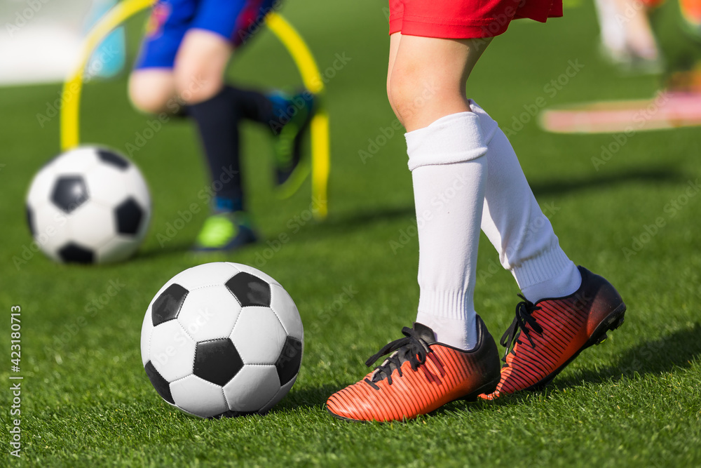 Closeup of child soccer player legs kicking ball. Kid running classic black and white football ball. School children on soccer playfield. Kids practicing sports on grass pitch