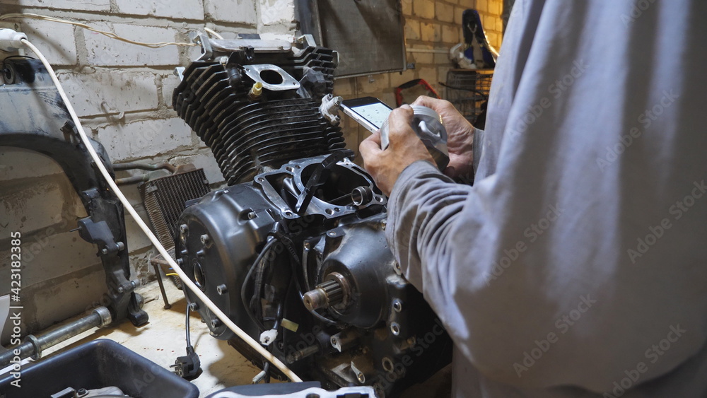 Male hands of mechanic searching properties and characteristics of vehicle detail on smartphone at garage. Professional repairman working at garage. Concept of maintenance service. Close up Slow mo