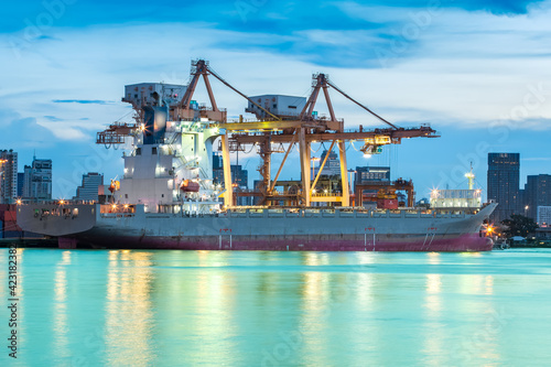 Container Cargo freight ship with working crane loading bridge in shipyard at dusk for Logistic Import Export background