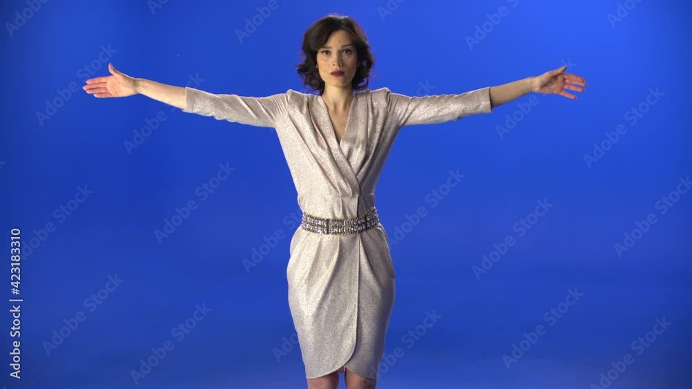 beautiful woman in a dress spreads her arms on a blue background in the studio. beautiful woman in a dress spreads her arms on a blue background in the studio.