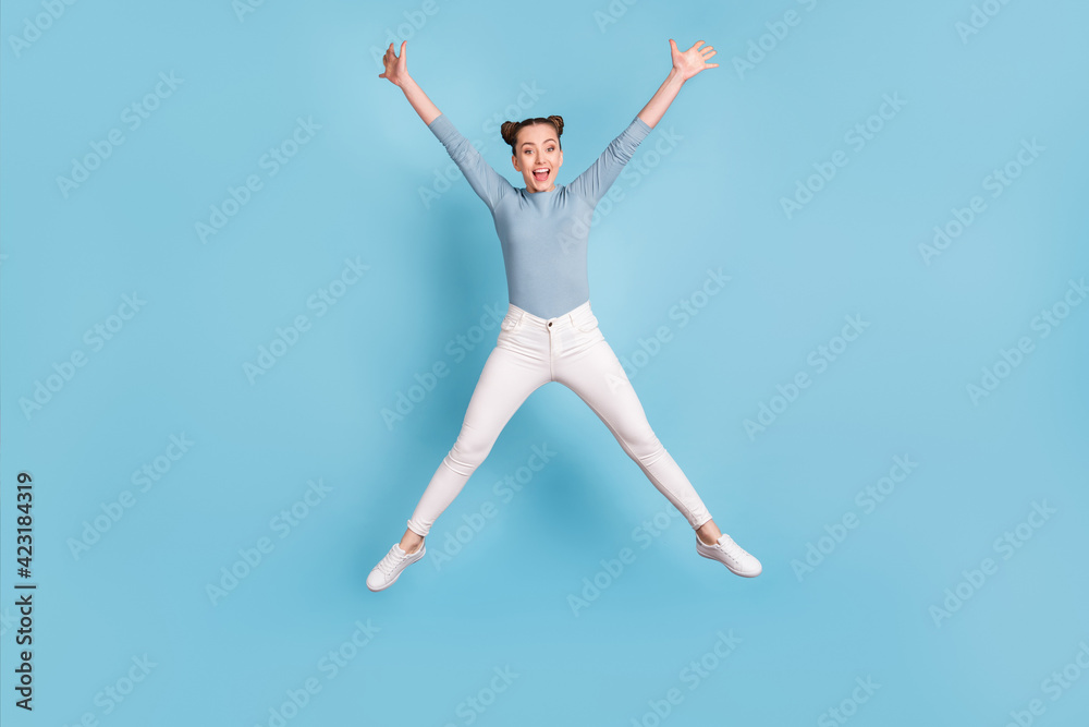 Full length photo of positive pretty young girl jump up air star pose isolated on blue color background Full length photo of positive pretty young girl jump up air star pose isolated on blue color background