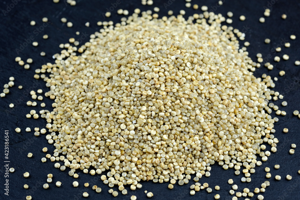 Heap of raw quinoa seeds on a black background. White quinoa close-up.