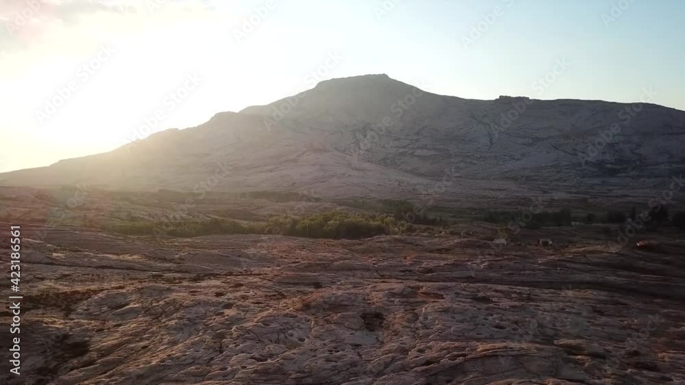 Dawn over frozen lava and mountains. Huge rocks and a gorge cast a shadow from the sun. Grass and trees grow in places. Houses are visible. Clouds in sky and bright rays of the sun. Beautiful gorge.