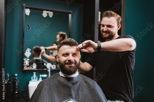 Happy young bearded male client of barbershop getting haircut