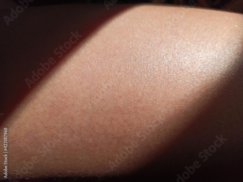 Thigh of a girl with a ray of sun. Close-up tanned skin in the shade.