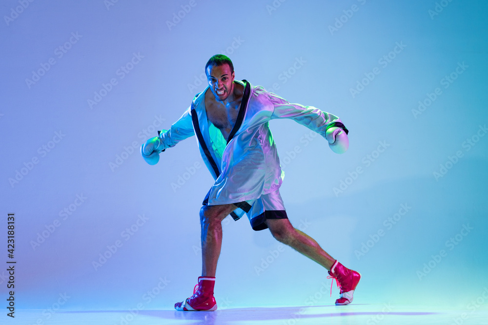 Obraz premium High-fashion styled man in white outfit pacticing box isolted over gradient background in neon light