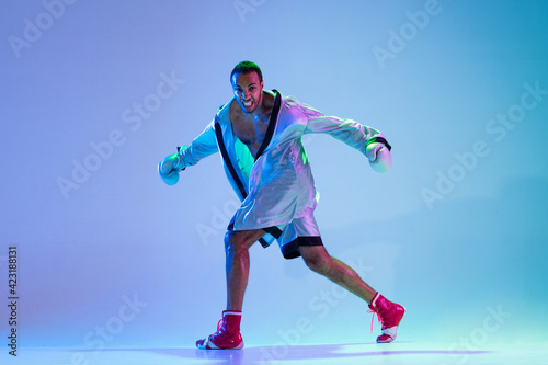 High-fashion styled man in white outfit pacticing box isolted over gradient background in neon light