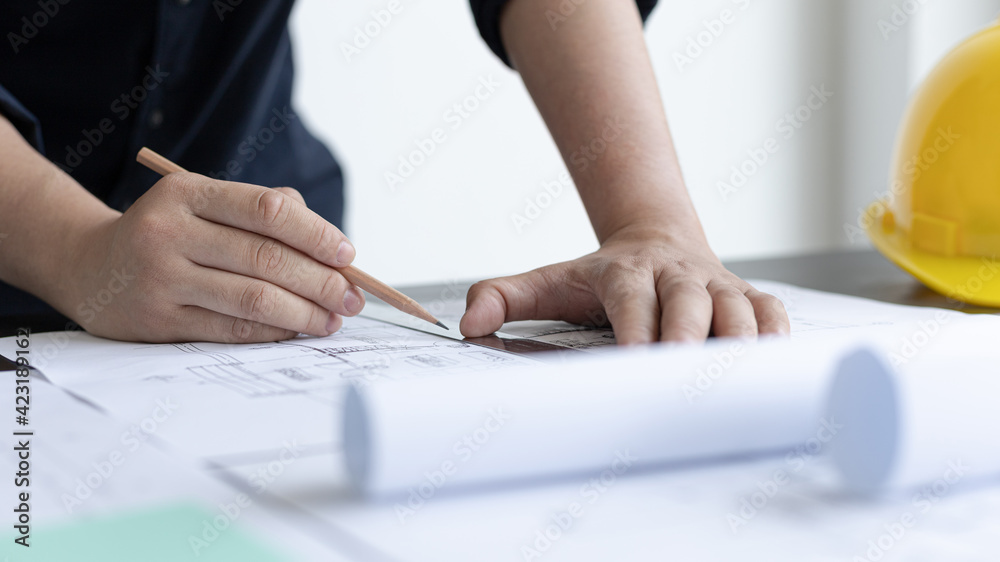 Architectural building design and construction plans with blueprints, Young man was designing a building or architecture with a ruler, pen, pencil, tape measure, architect hat. Architectural building design and construction plans with blueprints, Young man was designing a building or architecture with a ruler, pen, pencil, tape measure, architect hat.