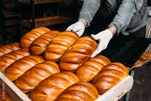 a man puts freshly baked bread on a tray. Baker puts a tray with fresh pastries on the shelf against the background of a bakery or bread factory.