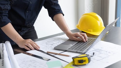 Young man with a laptop plotting a system of building structures in blueprints, Architects or engineers are designing buildings using computers to calculate the physical structure to be correct.