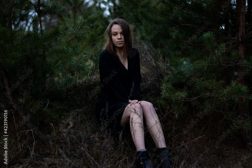 young brunette woman with short hair in a black dress near the pines