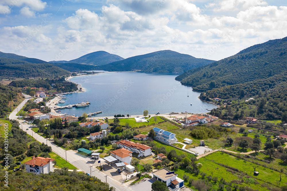 Top drone view from above to fairytale hills valley with round blue lake, red roof tiles country houses, summer green gardens, white clouds, sunny sky surrounding environment