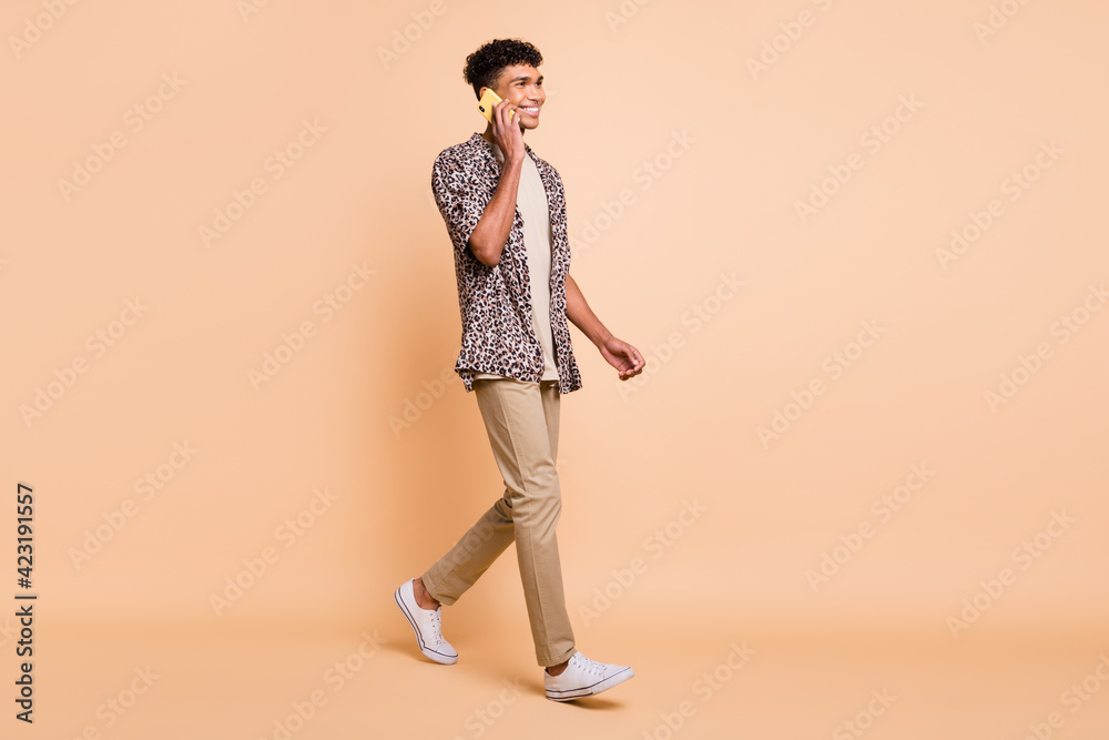 Full size profile photo of brunet optimistic guy going talk telephone wear modern shirt trousers sneakers isolated on beige background Full size profile photo of brunet optimistic guy going talk telephone wear modern shirt trousers sneakers isolated on beige background