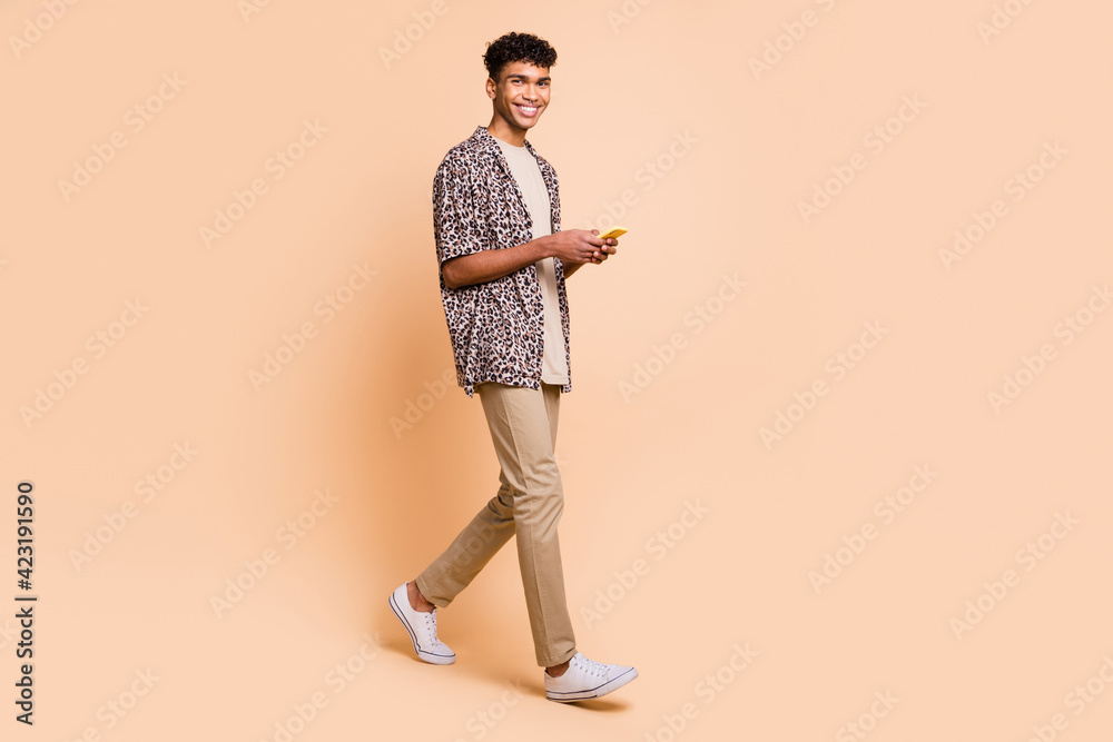 Full size profile portrait of handsome dark skin guy walking look camera have good mood isolated on beige color background