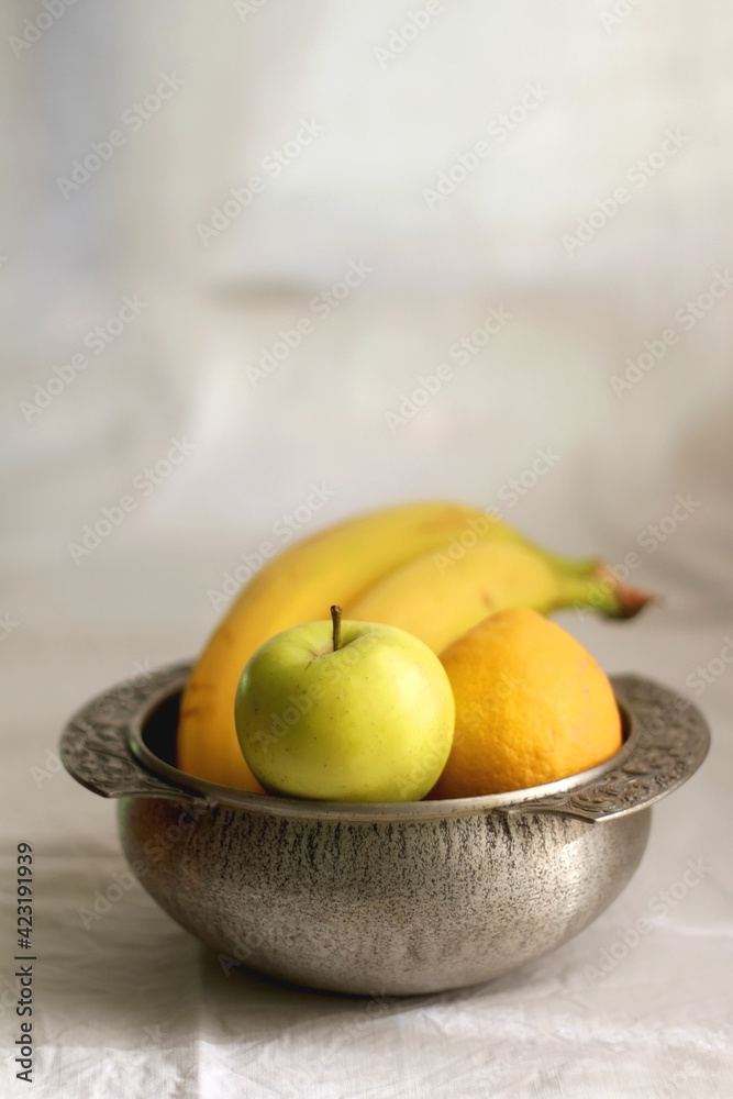Antique bowl with bananas, apples and lemons. Selective focus, white textile background.