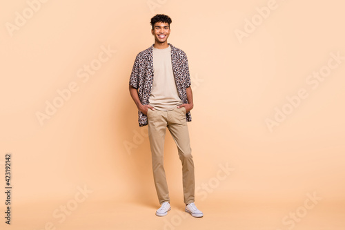 Full size portrait of friendly dark skin person put hands in pockets look camera isolated on beige color background