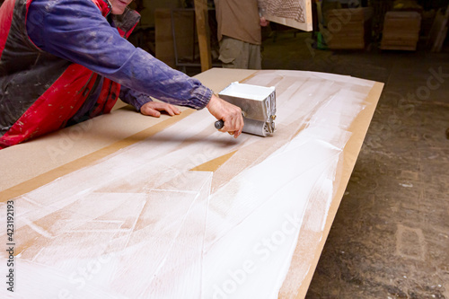 Carpenter smears the plywood with hand roller tool, spreader for evenly application of glue on the wooden surface