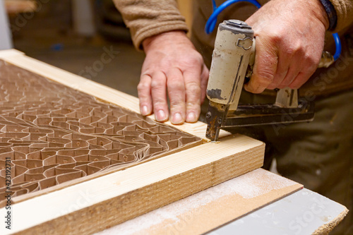 Carpenter assembles boards on the door frame with pneumatic stapler photo