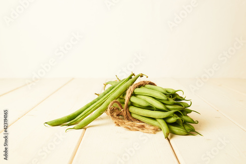 bunch of raw green beans tied up with a string on white wooden table