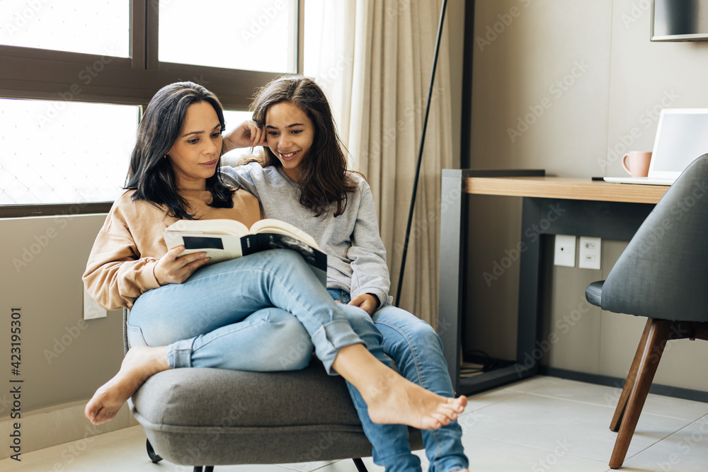Single parenthood. Mother and daughter reading a book together at home. Single parenthood. Mother and daughter reading a book together at home.