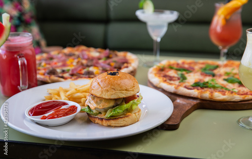 Variety of delicious fresh pizzas, snacks and drinks served on table in restaurant or cafe with focus on burger and french fries