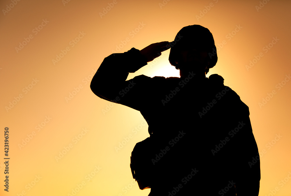 Silhouette of soldier in combat helmet and ammunition saluting on background of sunset sky. Army special forces fighter, Marines rifleman showing respect, greeting officer with salute gesture