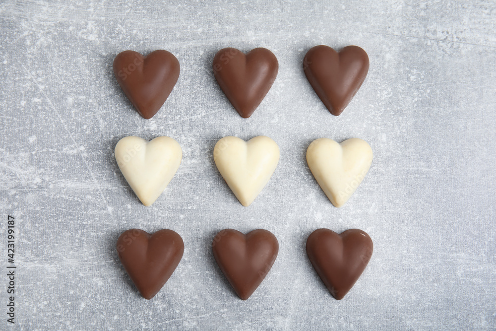 Obraz premium Tasty heart shaped chocolate candies on light grey table, flat lay. Happy Valentine's day